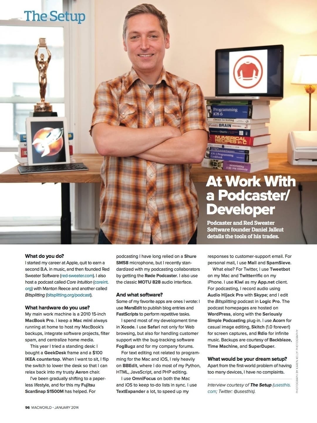 Picture of a full page of a traditional print magazine, where the top portion is a picture of a caucasian man standing, smiling, with his arms crossed, looking straight at the camera. He is surrounded by a staged workplace desk in his home office, with a stack of books and a Macworld award statue. The bottom portion of the image is interview text.