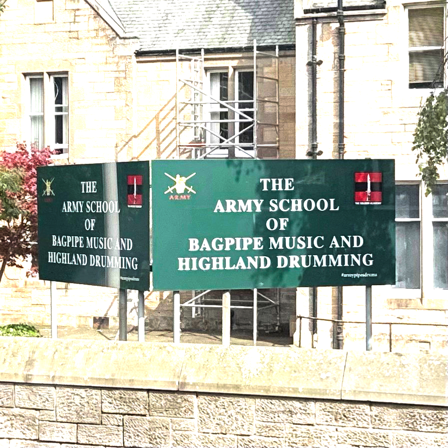 Sign in front of a stone building reading “The Army School of Bagpipe Music and Highland Drumming.”