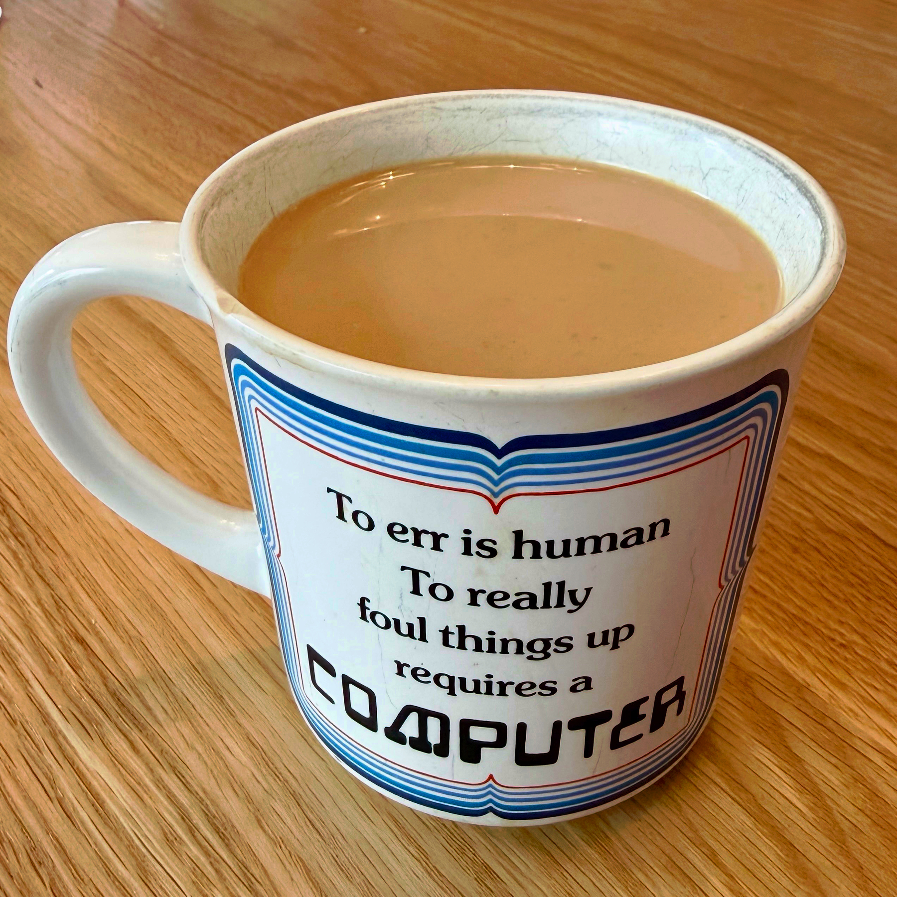  Coffee mug with a vintage ‘80s design, inscribed with the statement: “To err is human To really foul things up requires a COMPUTER”.