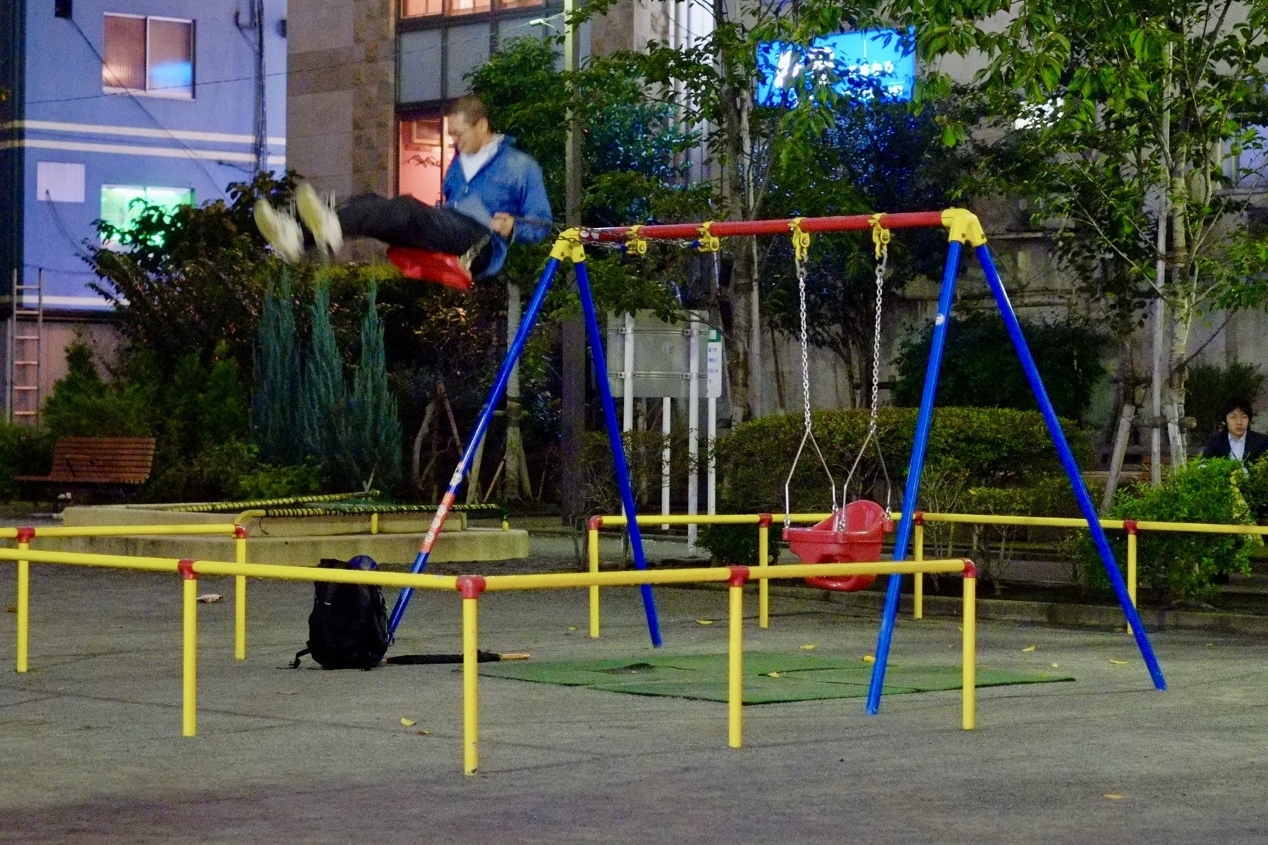 Adult man swings high on a childrens’ swingset at a park in Shimbashi Tokyo Japan. 