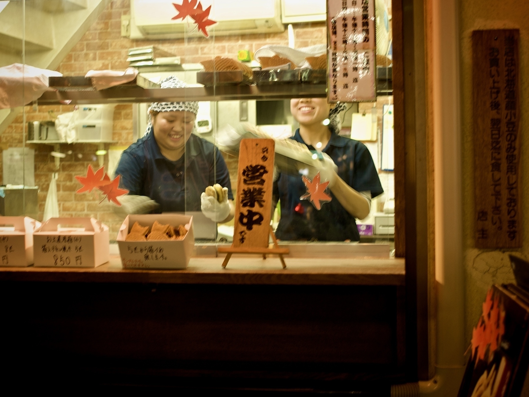 Female taiyaki sweet bean paste bun vendors looking happy as they work, through the window of their shop in Ginza Tokyo. 