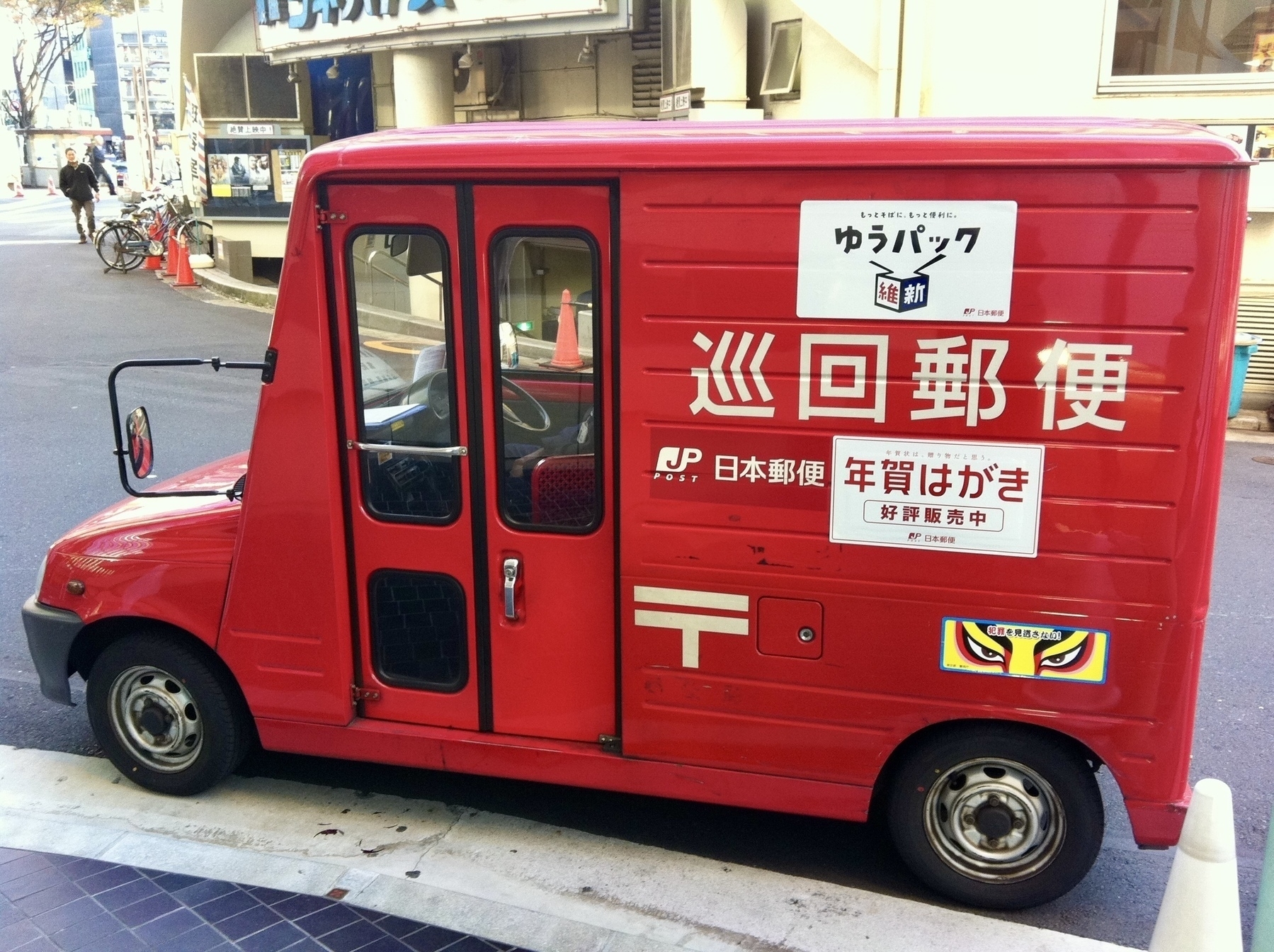 Small red Japan Post mail truck from the side. 