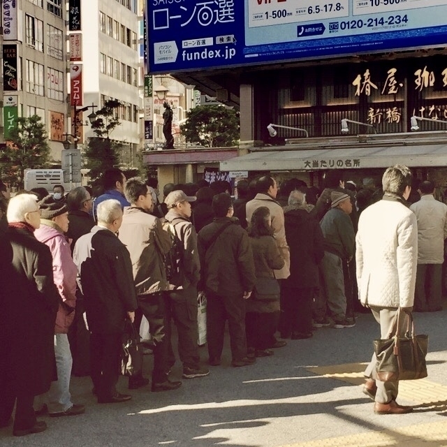 Long queue of people outside a Tokyo building, all bundled up against the winter cold. 