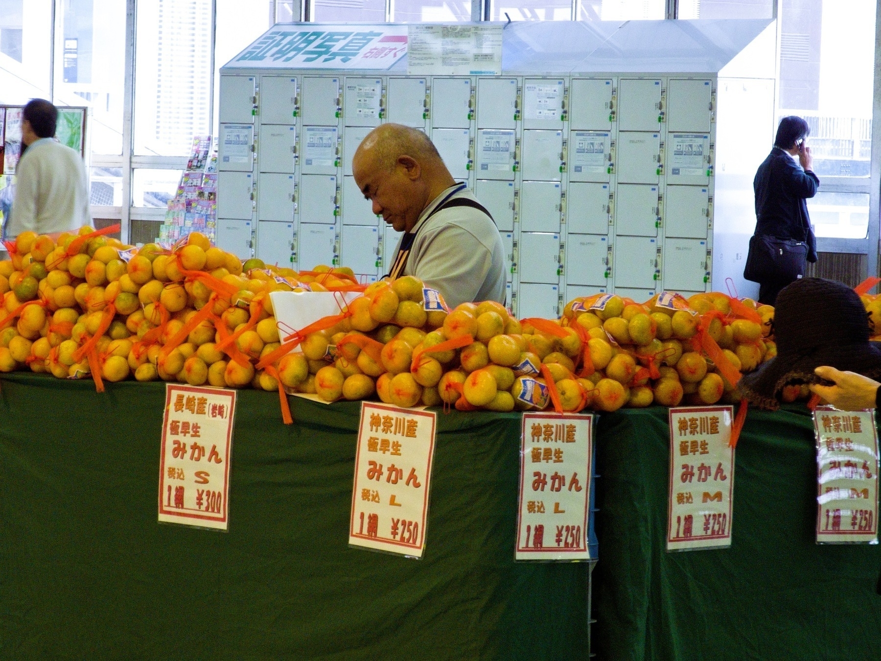 Mikan orange seller asleep at his stall in front of a locker bank at a train station in Japan. 