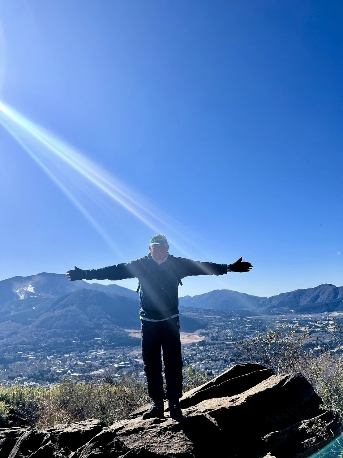 Man standing on a rock part way up a mountain, with his arms outstretched. 