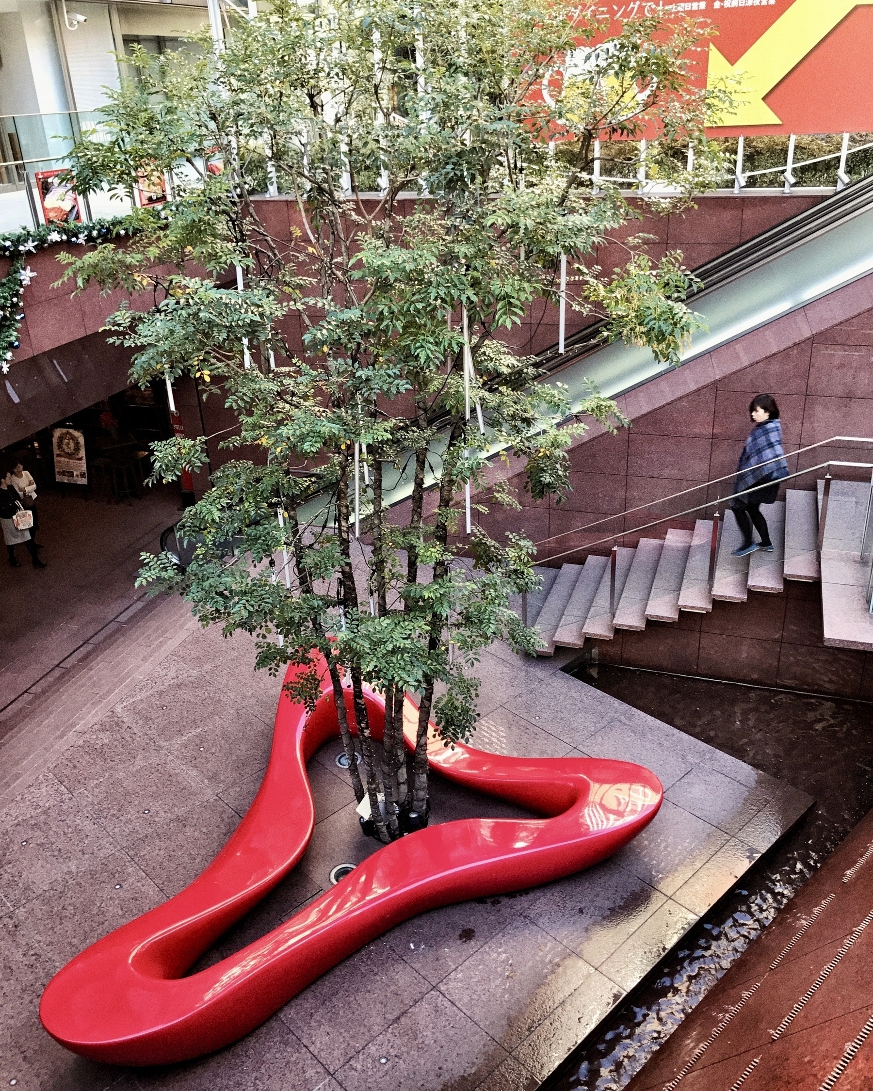 Red bench sculpture object in Tokyo courtyard surrounds a lonely tree. 