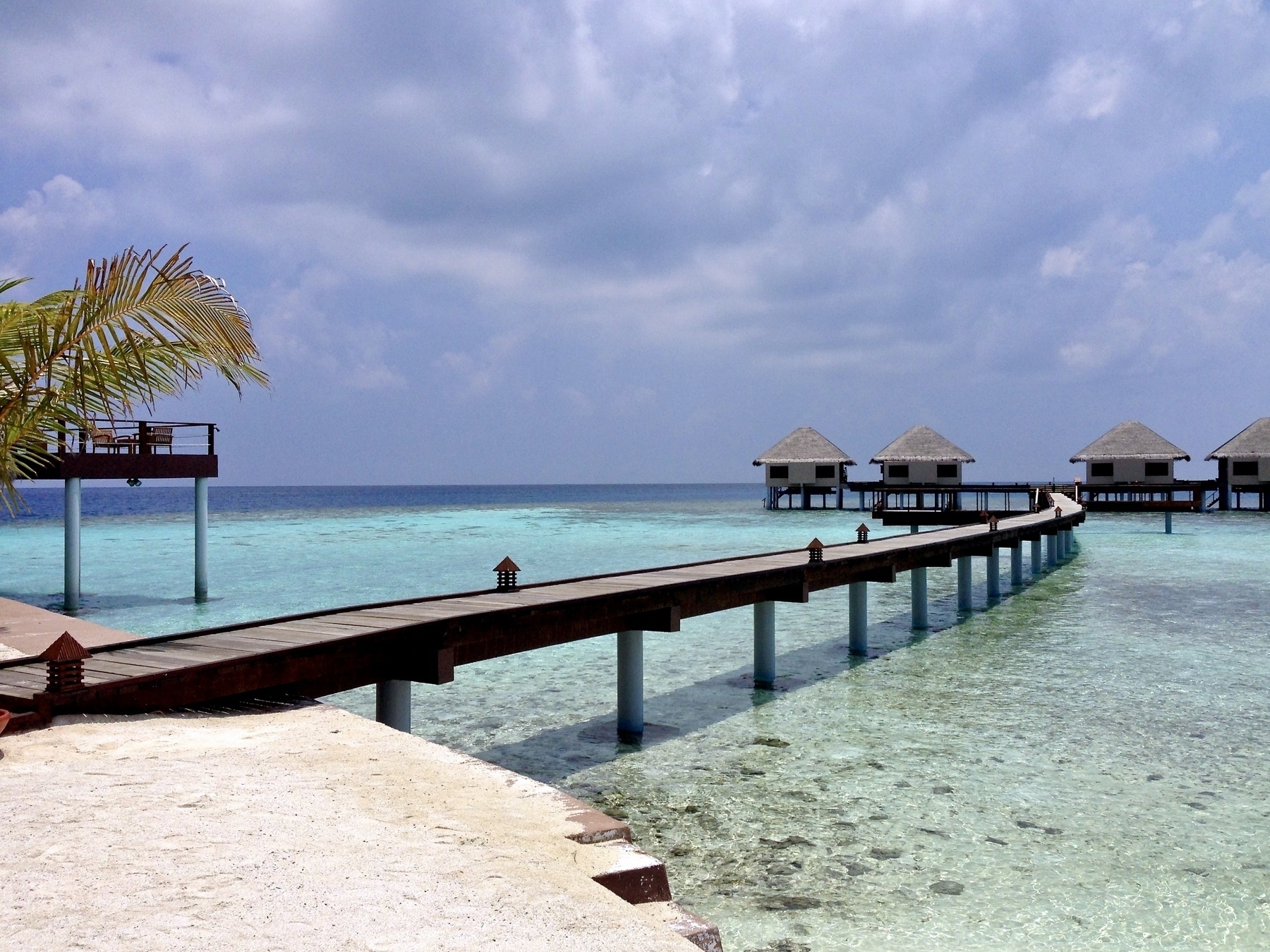 Photo of a pier over the ocean leading to huts, in the Maldives
