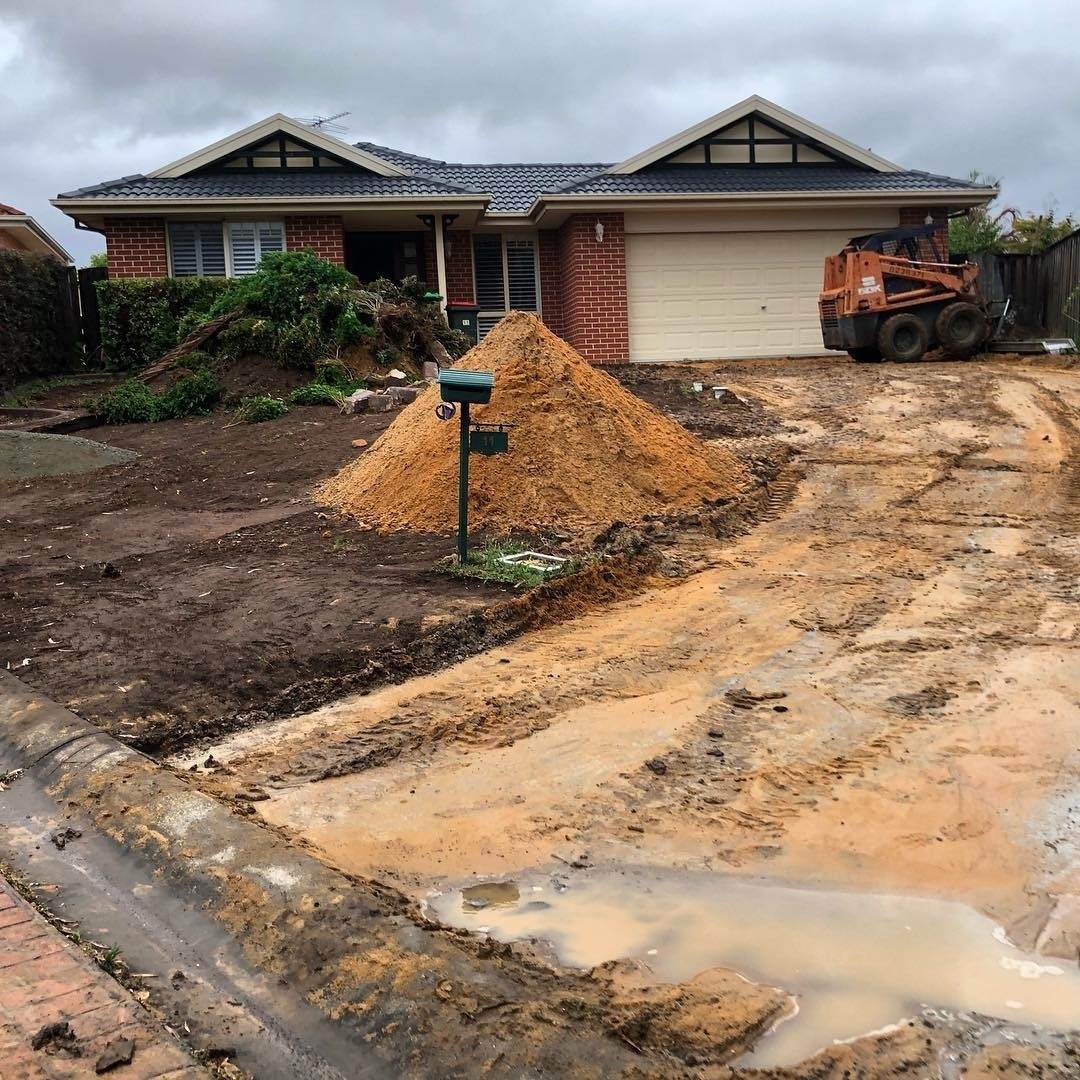 A house with a ripped up front driveway, piles of dirt and ripped up grass and a large puddle.