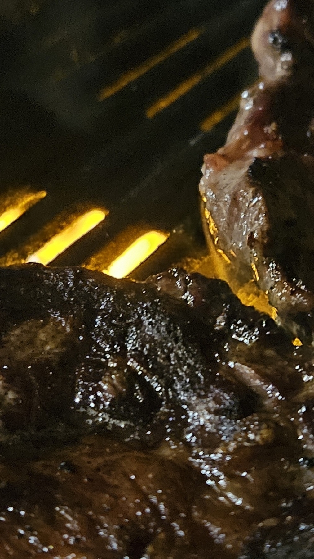 Close up of a steak cooking on a barbecue, with flames behind the grill. 