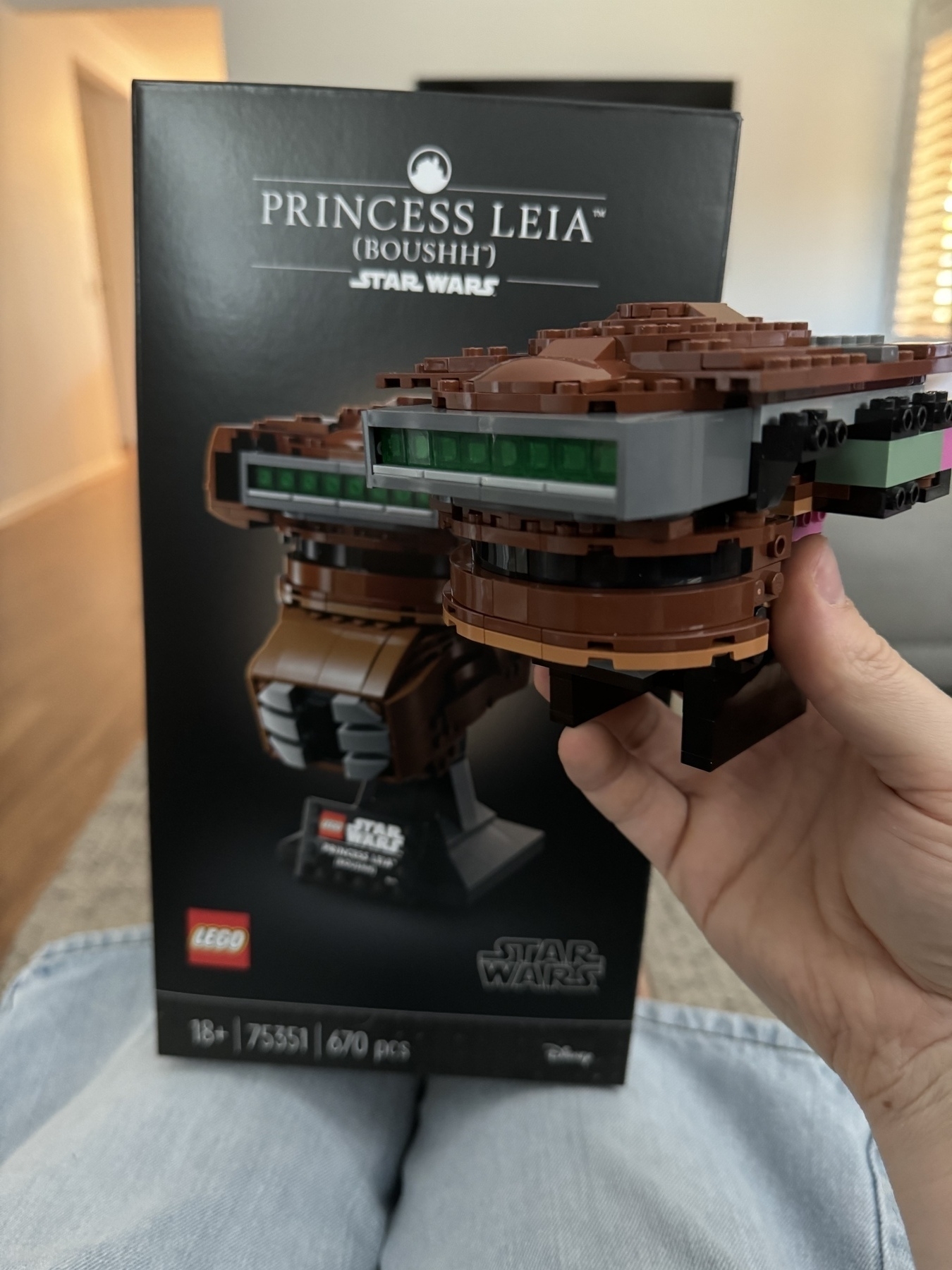 The Star Wars Lego Princess Leia Boushh helmet partially constructed, being held up in front of the box showing the completed product. 