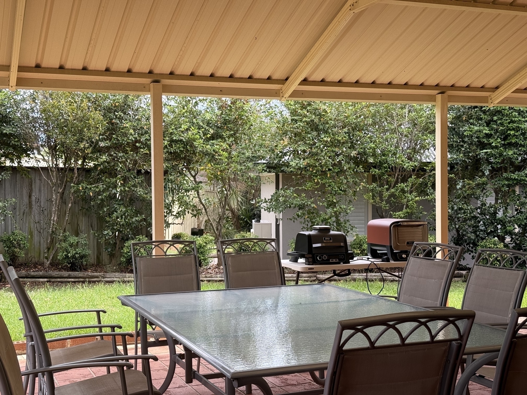 The view from my desk with an outdoor table, a bbq and trees, but only half a fence as it is being removed. 