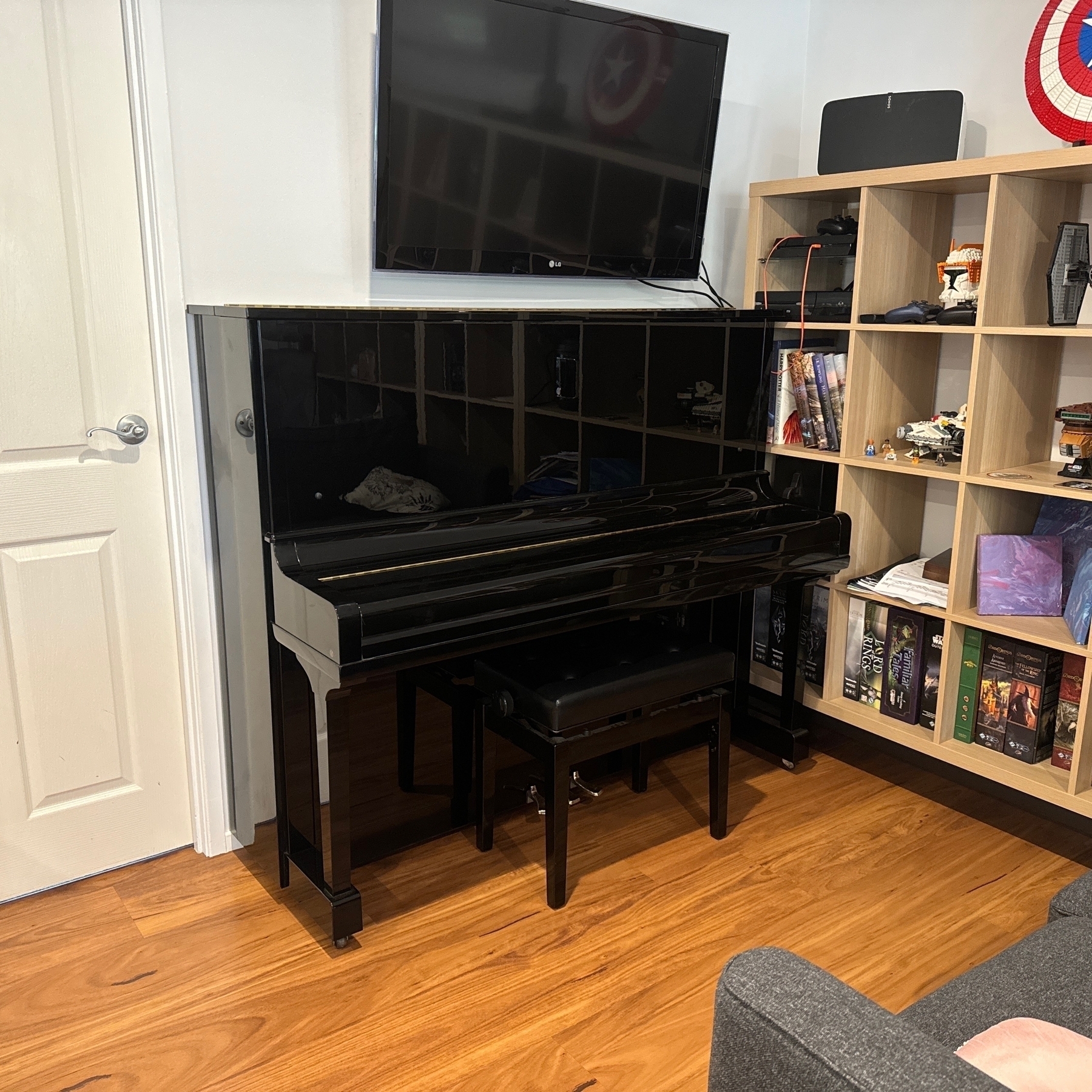 A black Yamaha piano under a wall mounted tv next to an ikea bookshelf.