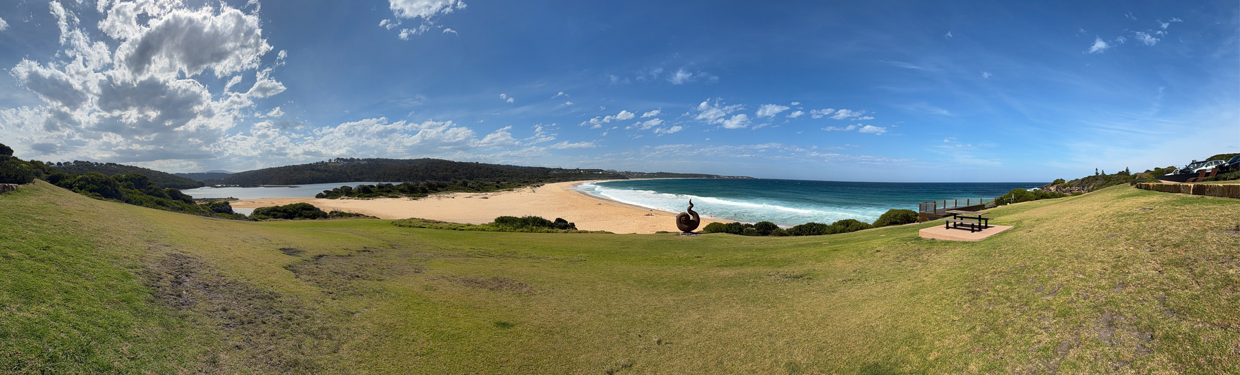 A panorama of the ocean and beach from a grassy hill