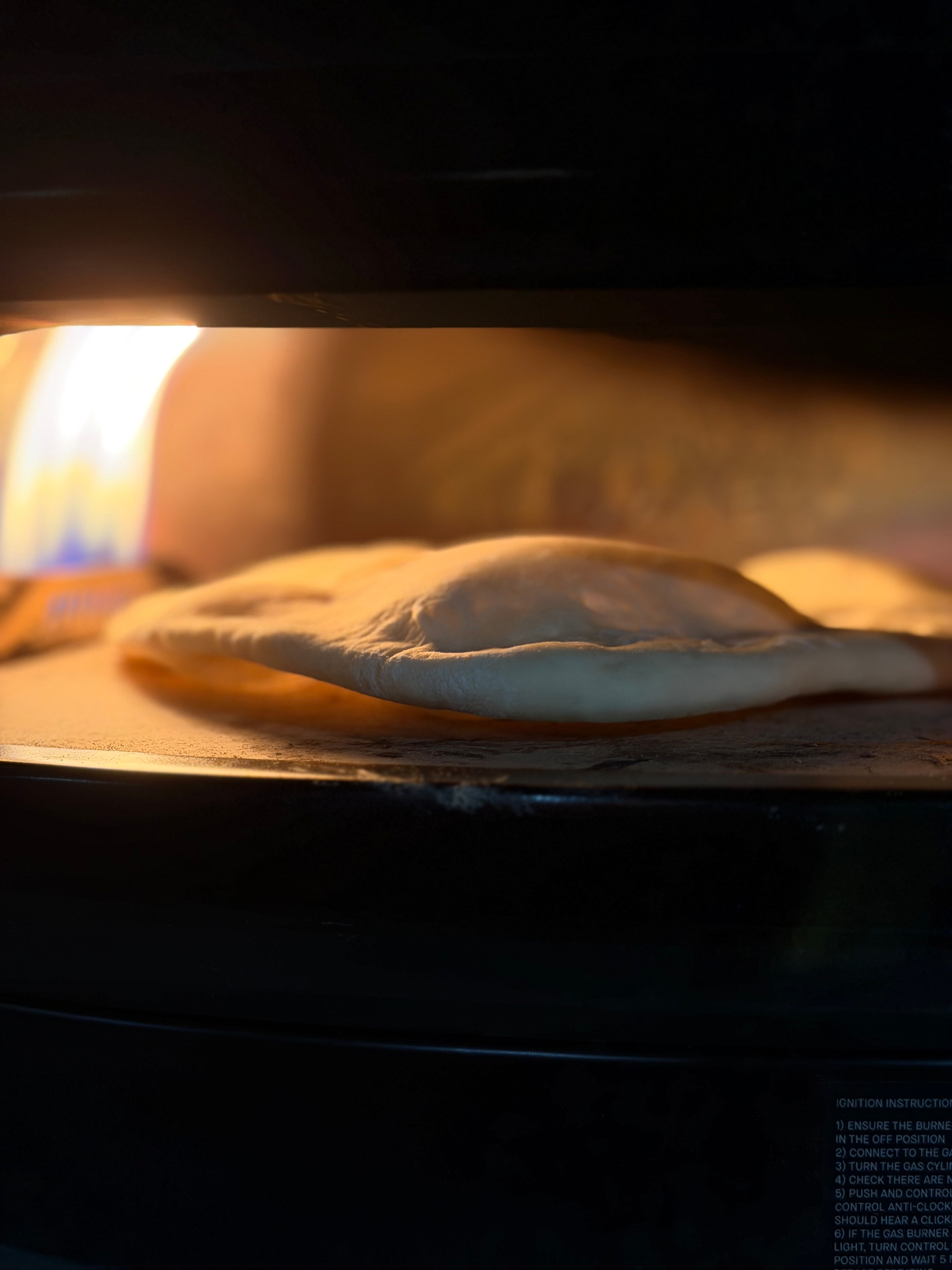 A flatbread is baking in an oven, puffing up near an open flame.