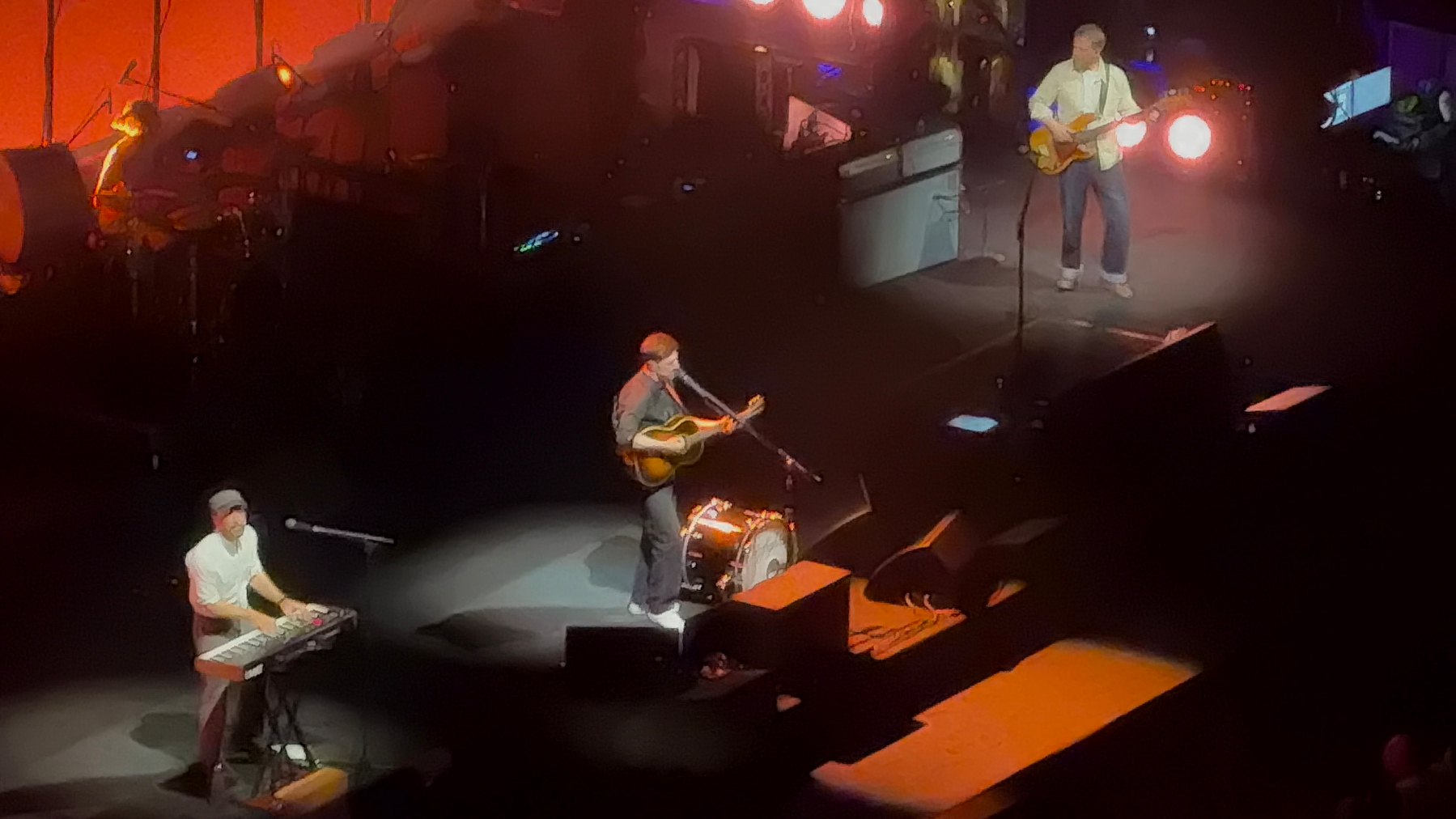 A band is performing on stage, with musicians playing guitars and a keyboard under colorful lights.