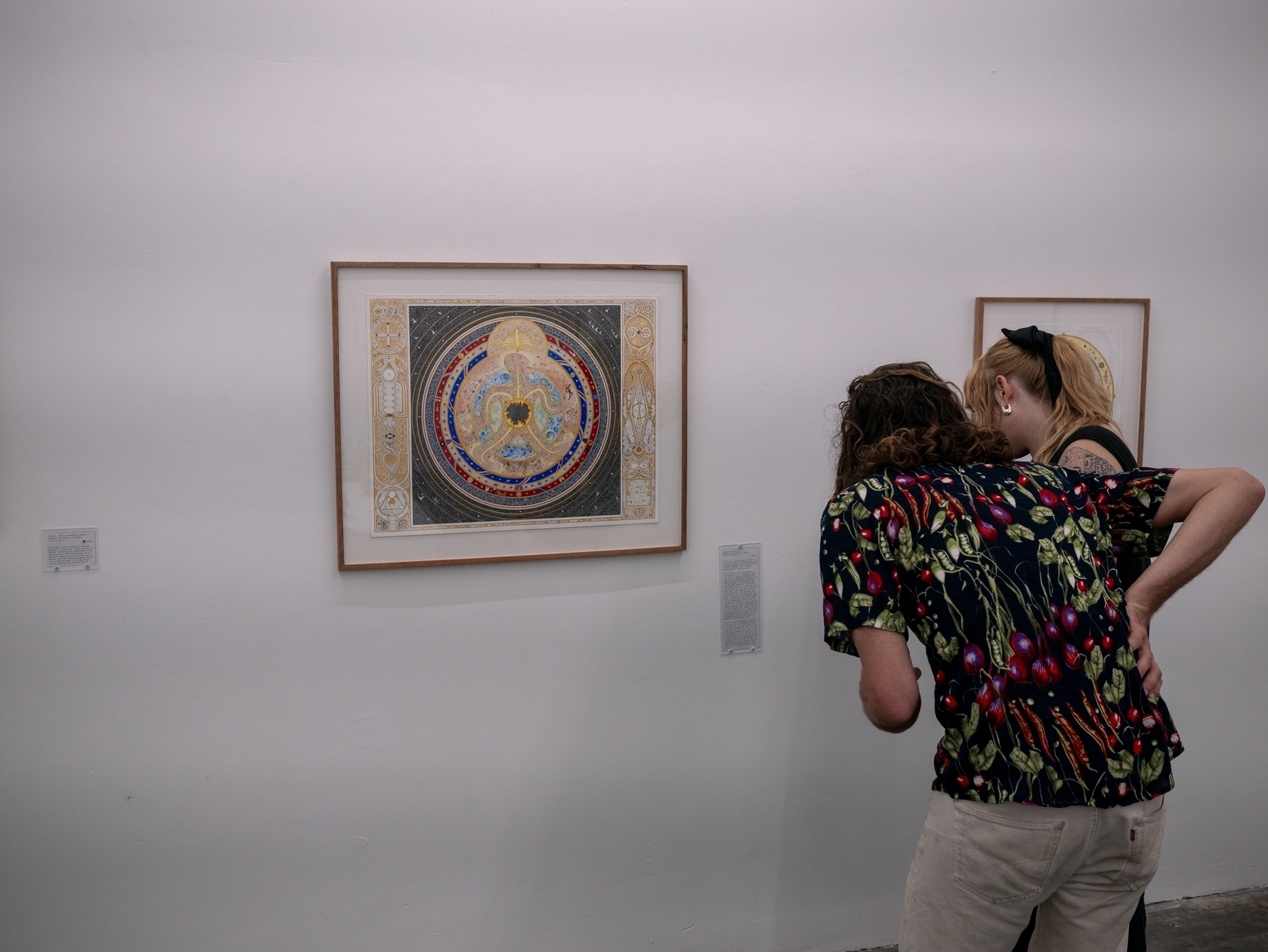 A photo of two visitors peering to read the wall text of a painting
