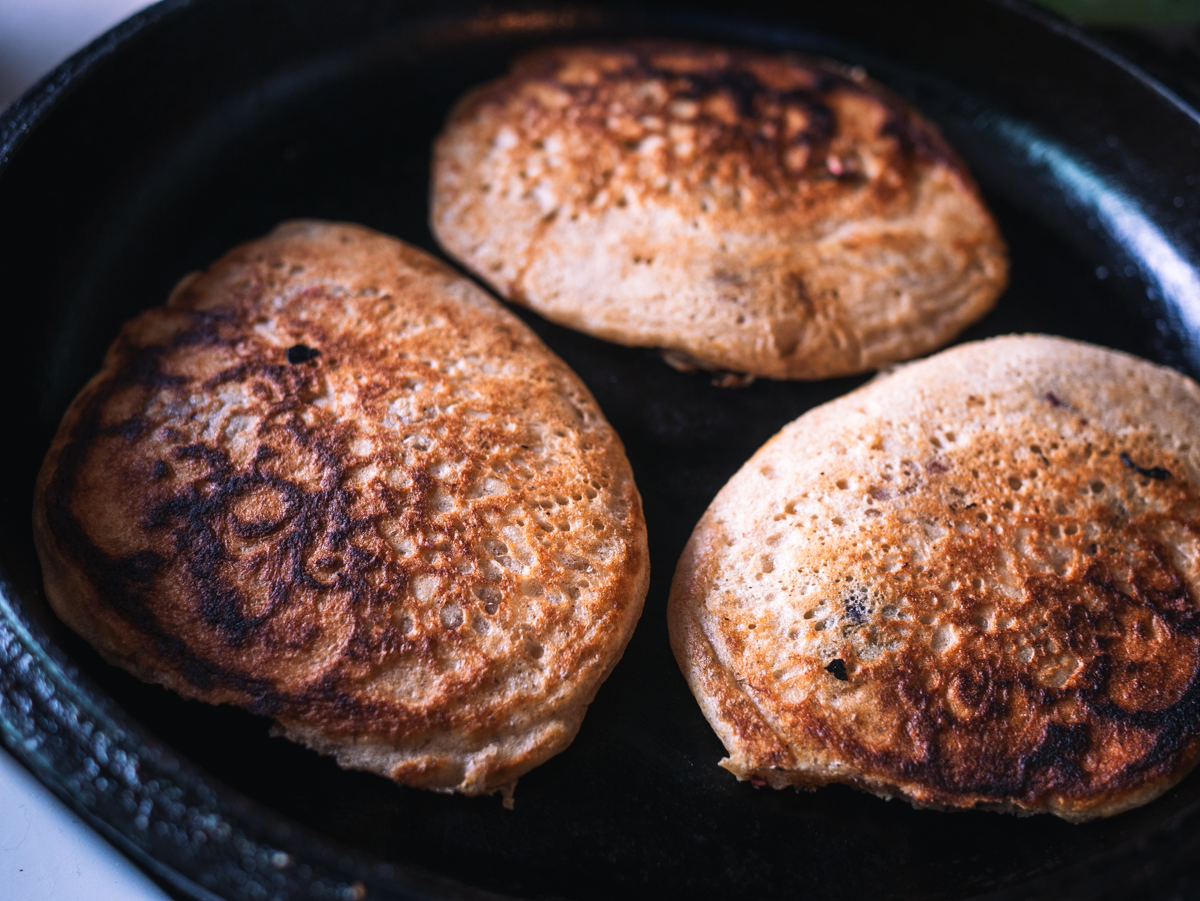 A photograph of three pancakes in a cast iron pan.
