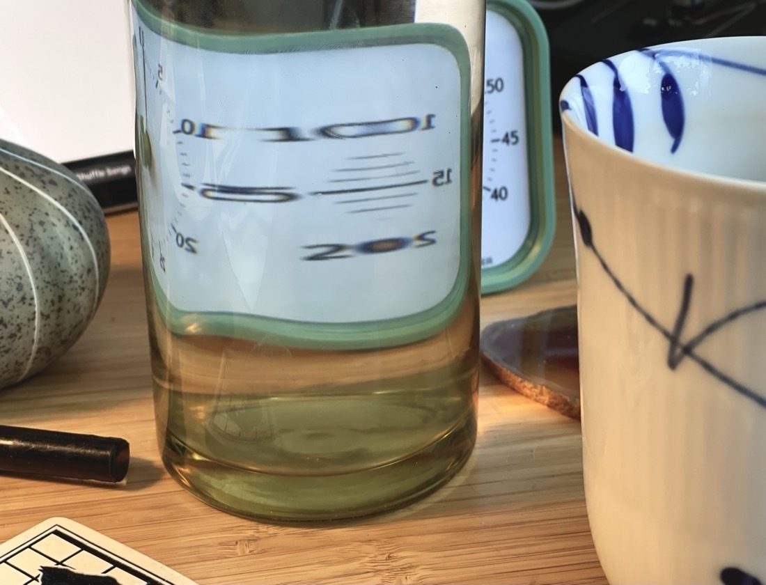 A photo of items on a desk, with distortion through a water carafe.