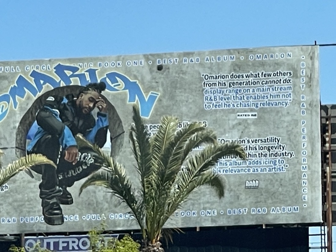 A photo of a billboard showing an artist named Omarion crouching in a glamorous pose, surrounded by blurbs praising his music.