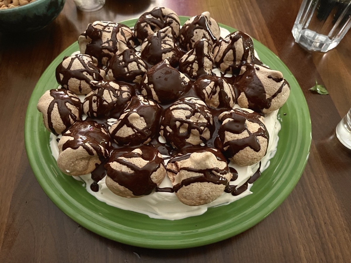 Photo of a cake with meringues on top, drizzled with chocolate.