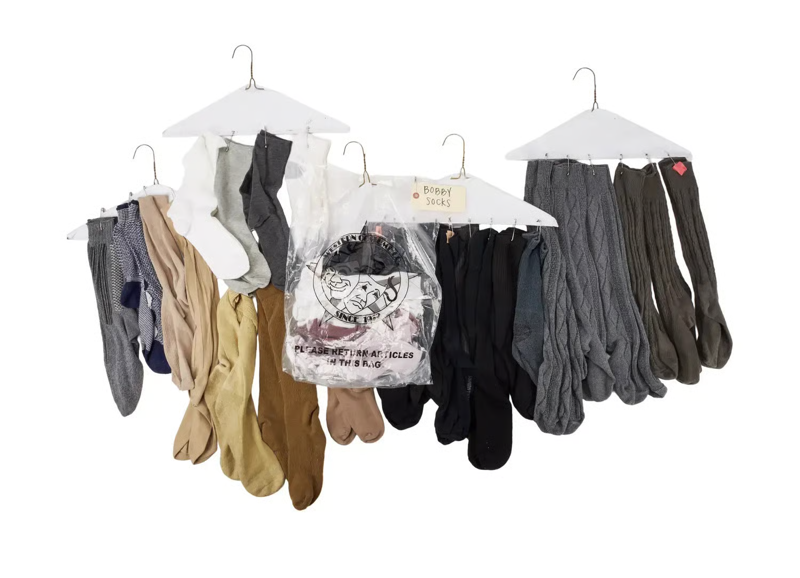 A photo of many socks in neutral tones hanging from drycleaning hangers, against a white background