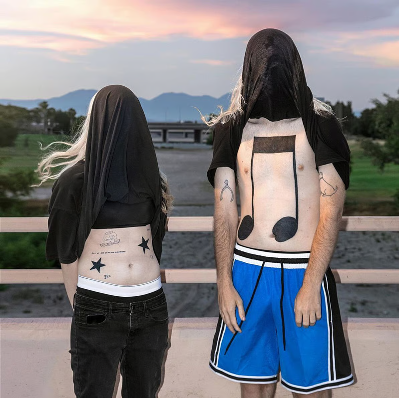 The album cover for 10000 Gecs which shows two figures who have their t-shirts pulled over their faces, revealing tattoos on their chests and stomachs.