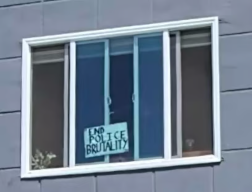 A blurry photo of a window with a sign in it reading "End Police Brutality"