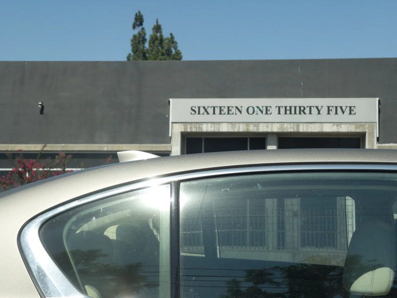 A photo taken from a car showing a building with a sign that reads "SIXTEEN ONE THIRTY FIVE"