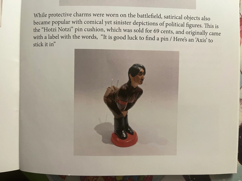 A picture of a book page open to a figure showing a Hitler pincushion; Hitler is bent at the waist and pins are sticking into his rump