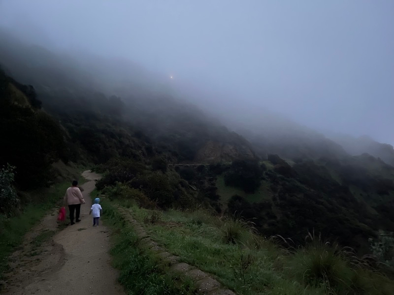 A photo of two people walking down a mountain path in dim fog.