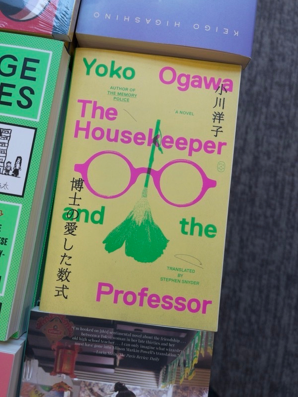 The cover of The Housekeeper and the Professor, showing a pair of glasses and a mop, the text all in fluorescent green and pink.