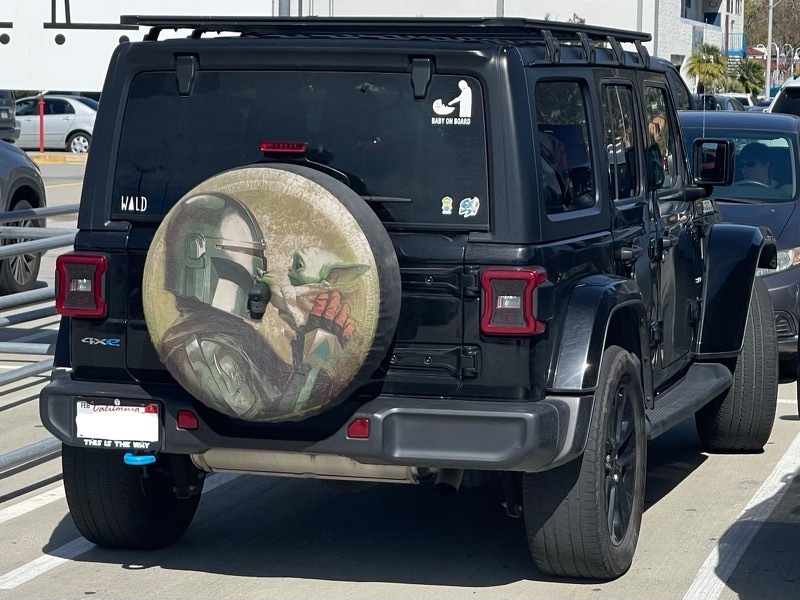 A photo of a Jeep with a Mandalorian spare tire cover and a "The Child on Board" decal and a "This Is the Way" license plate holder