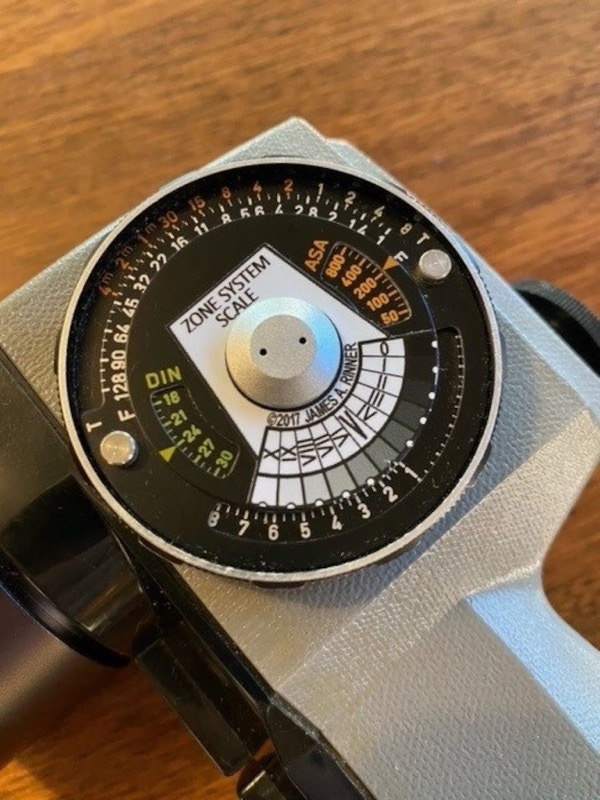 A close-up photo of a Pentax Spotmeter V's exposure calculator with a sticker reading "ZONE SYSTEM SCALE" stuck over it