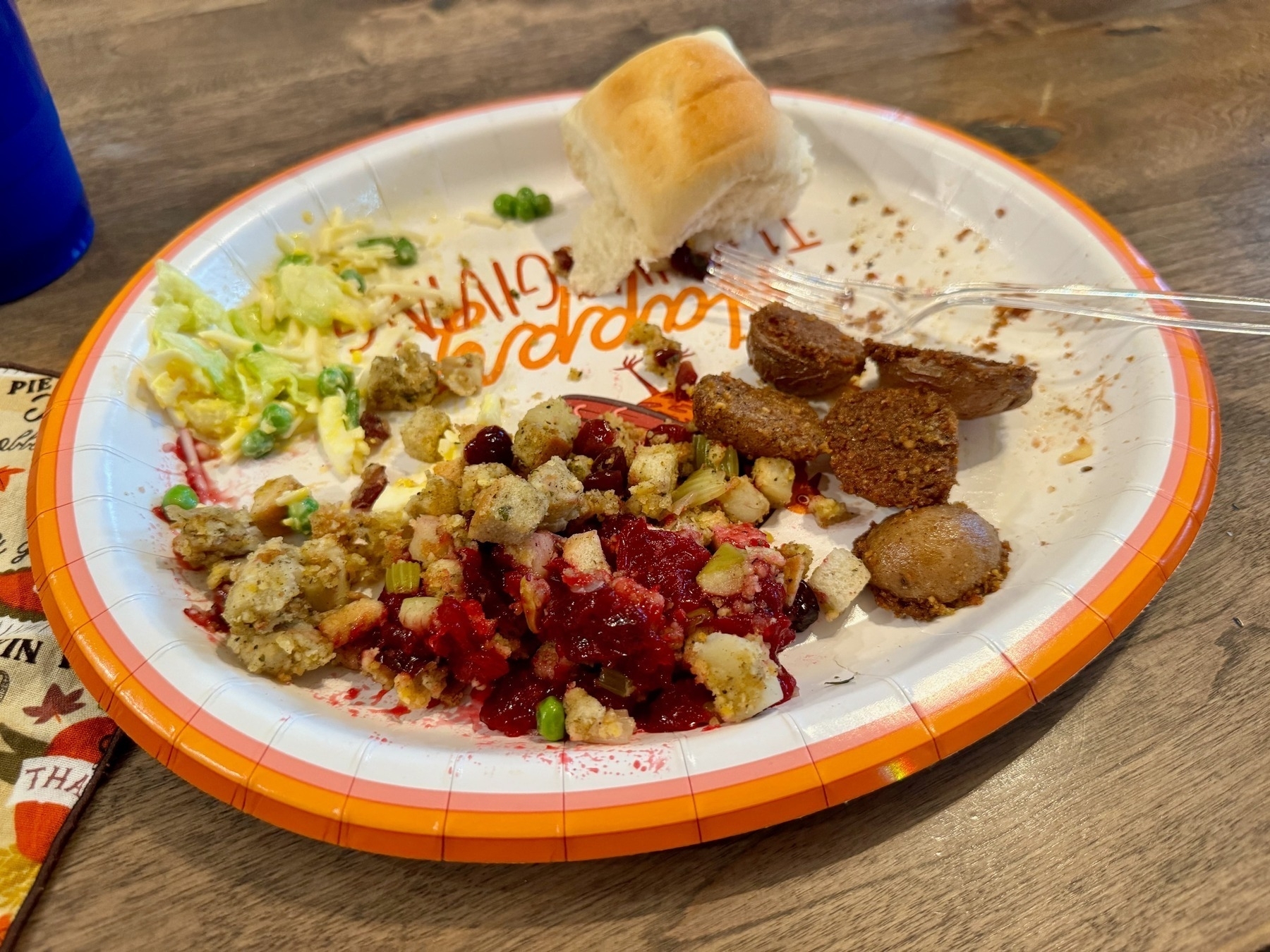 Various Thanksgiving food (stuffing / dressing, salad, potatoes, cranberry sauce, roll) on a paper plate, with a fork.