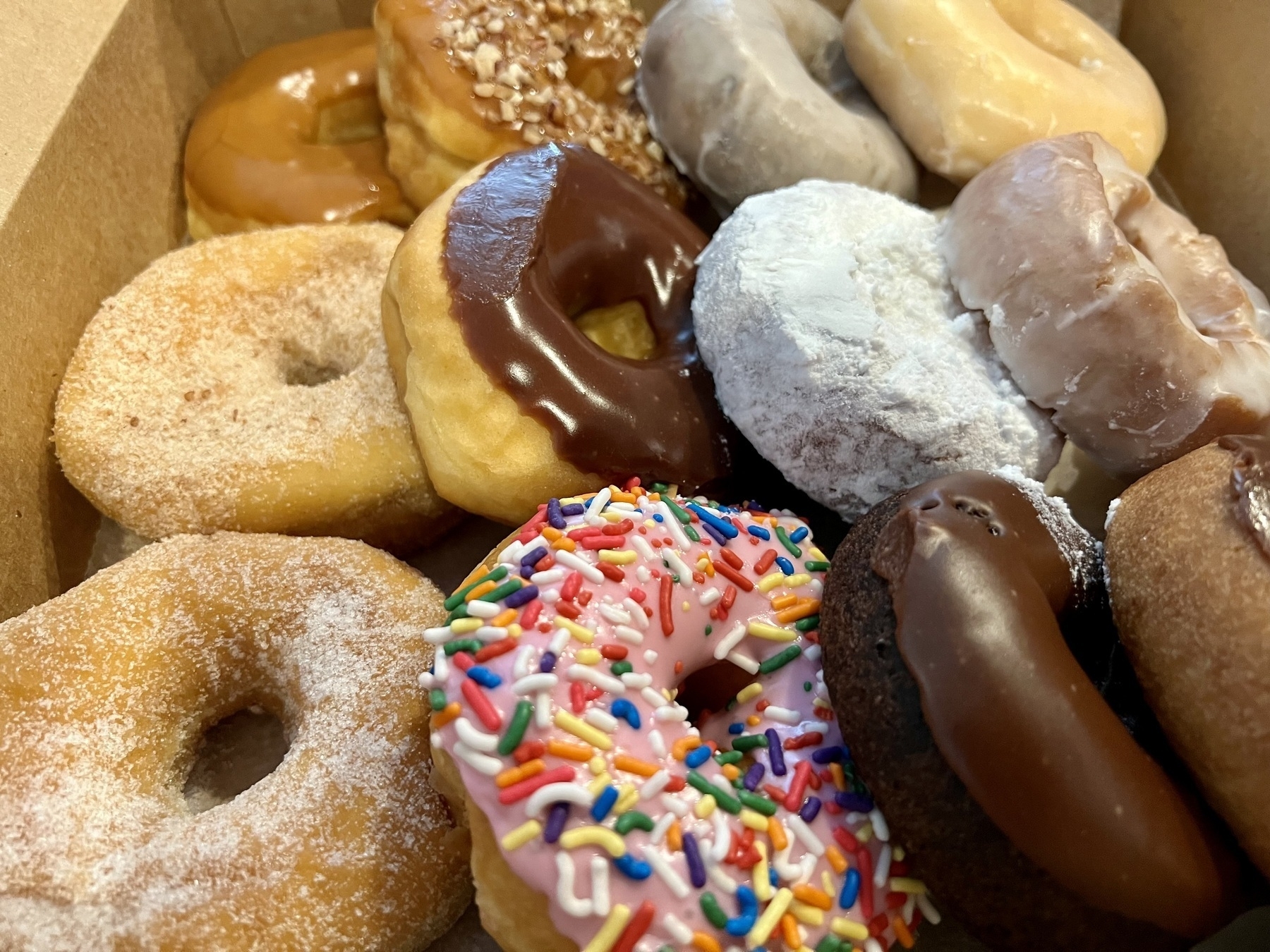 Collection of mixed donuts (some covered with sugar, some with sprinkes, some with a sugar-glaze, some with chocolate), four by three, for a total of twelve.