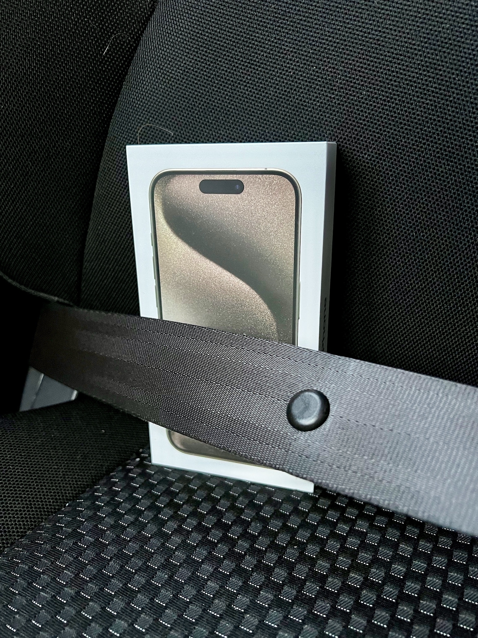 An iPhone 15 Pro box in on the seat of a car, behind a seatbelt.