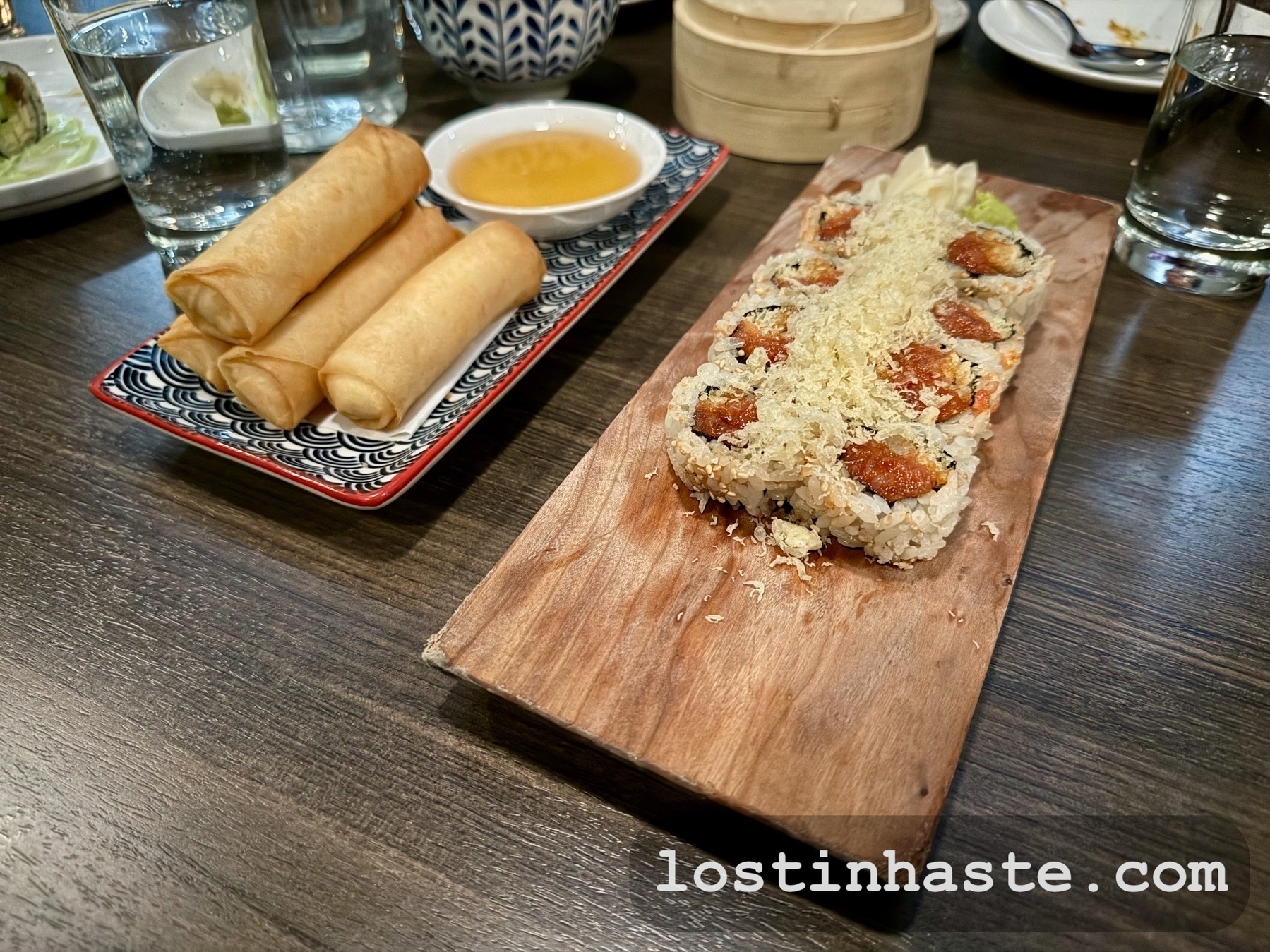 Roll of tuna sushi, horizontally cut, next to a stack of spring rolls on a different plate.