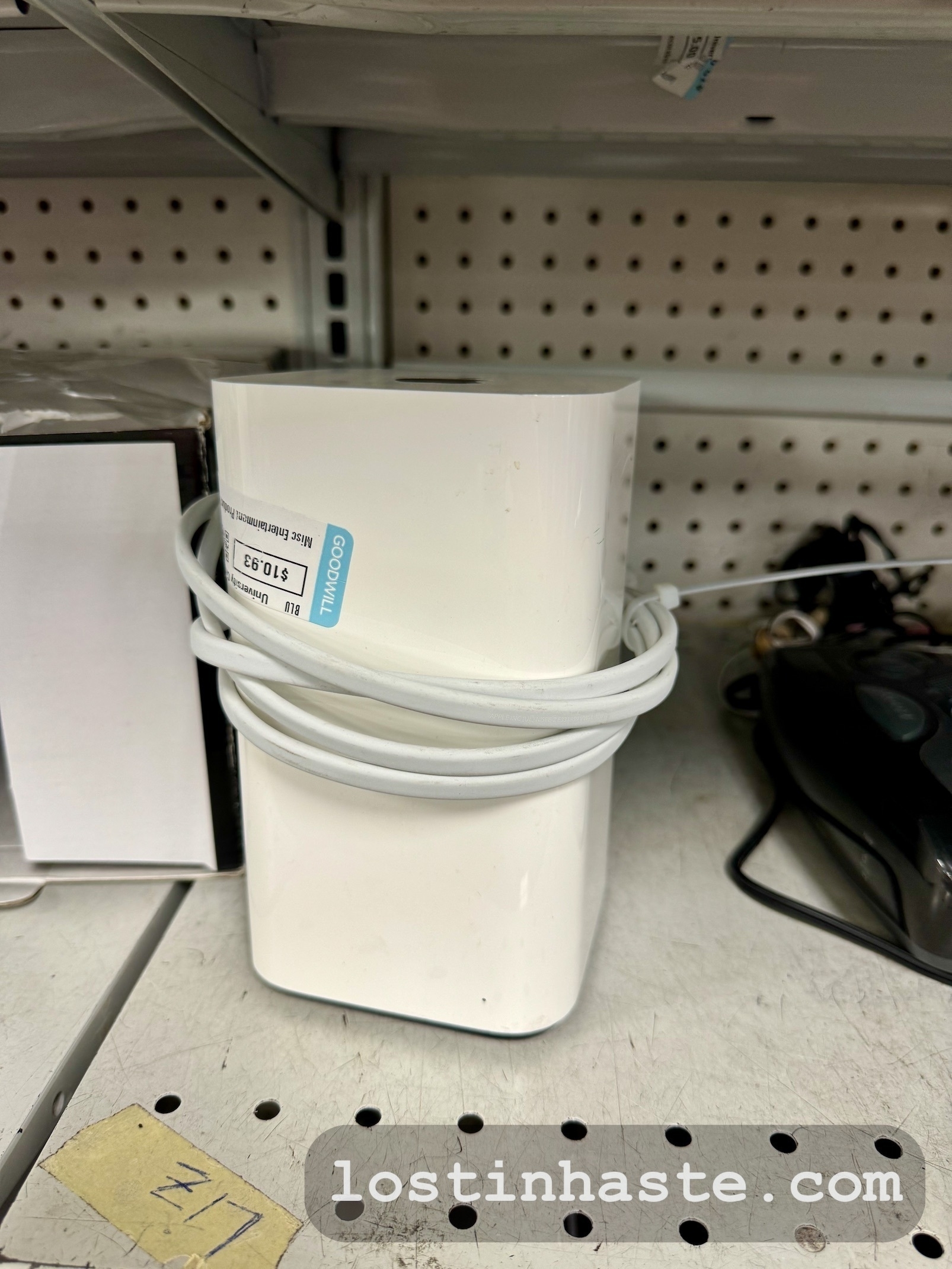 A white plastic cylinder nested with a coiled cord, on a metal shelf, with a website address, 'lostinhaste.com', superimposed in the foreground.