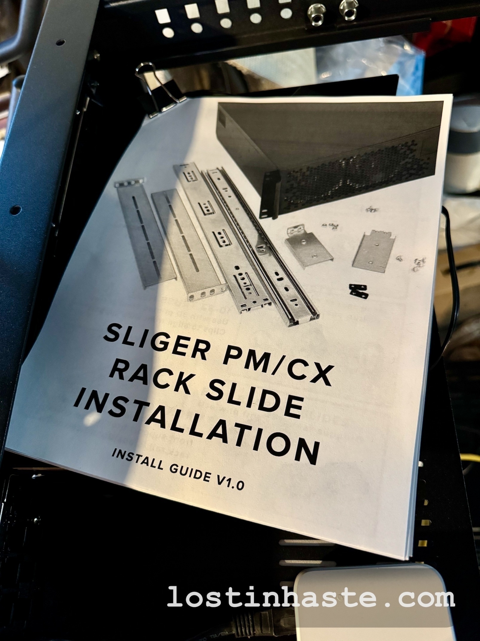 A manual titled 'SLIGER PM/CX RACK SLIDE INSTALLATION INSTALL GUIDE V1.0' rests on hardware parts, with the URL 'lostinthe.com' visible at the bottom.