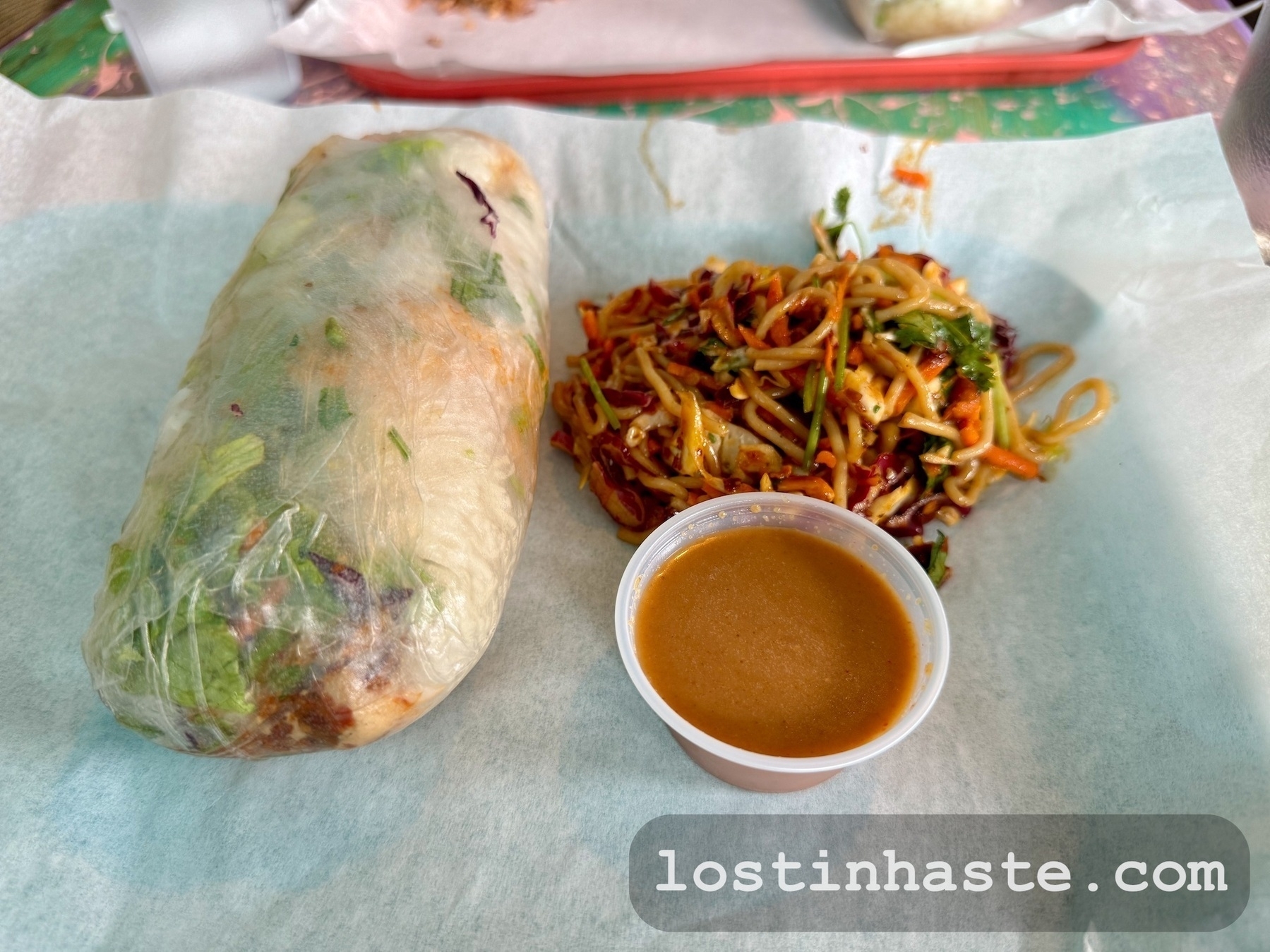 A fresh spring roll and spicy noodle salad served with peanut sauce on a tray.