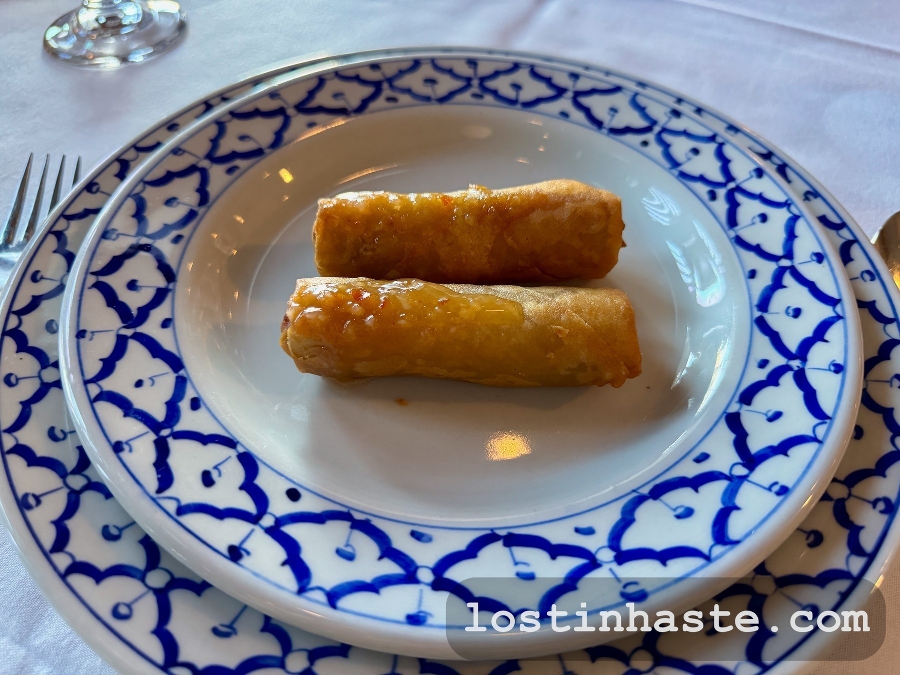 Two spring rolls are served on a decorative blue and white plate.