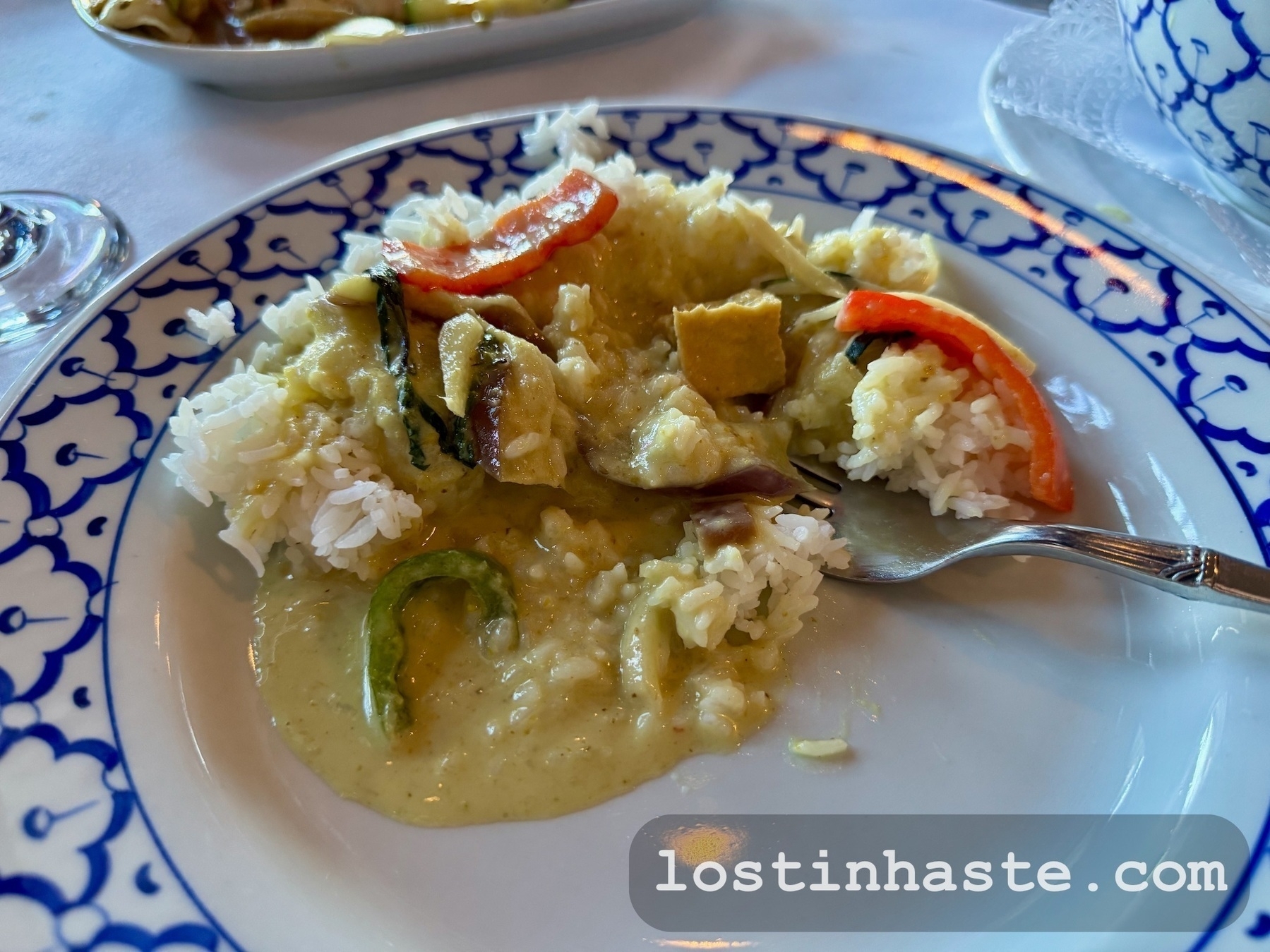 A plate of rice is topped with a creamy green curry sauce and garnished with various vegetables.