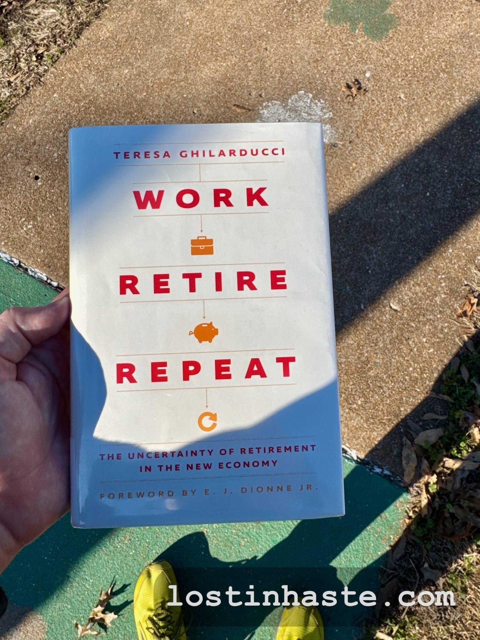 Auto-generated description: A person is holding a book titled Work Retire Repeat by Teresa Ghilarducci, featuring a subtitle about the uncertainty of retirement in the new economy, outdoors on a sunny day.