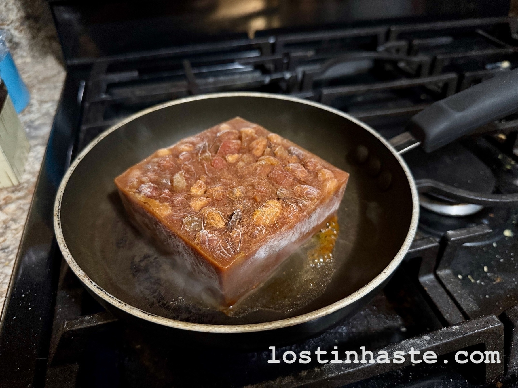 Auto-generated description: A large block of frozen curry is being heated in a frying pan on a stovetop.