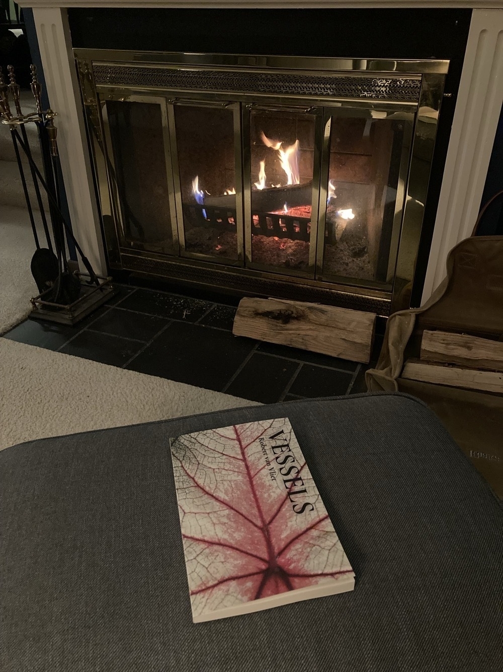 A copy of my book lying on an ottoman; a fire in the fireplace in the background