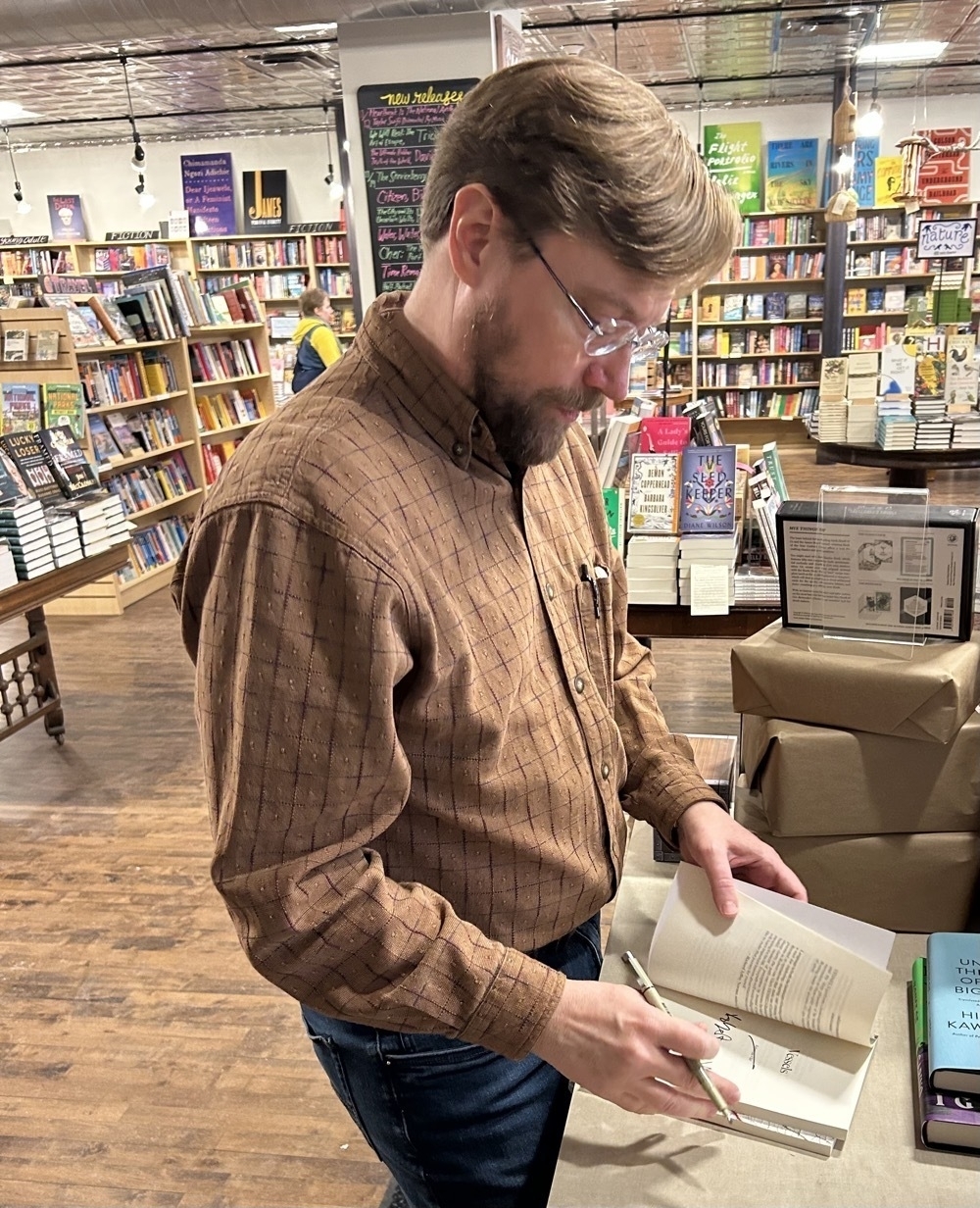 Your Humble Author signing a copy of Vessels, the bookstore in the background