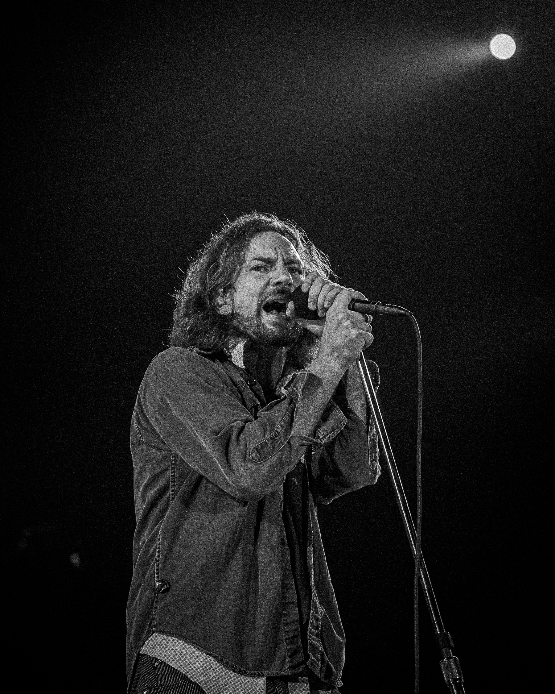 Eddie Vedder from Pearl Jam singing into a microphone on a stage, staring into the lens.