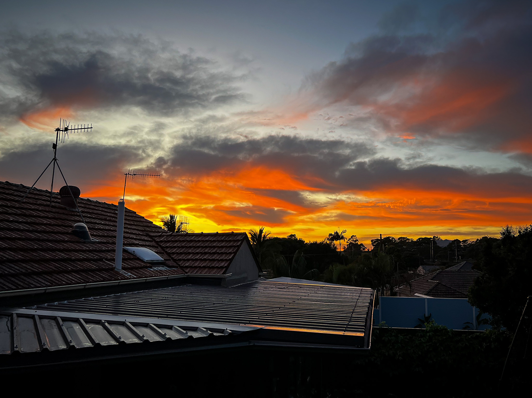 The sun rising and cutting golden light through the clouds over suburban rooftops.
