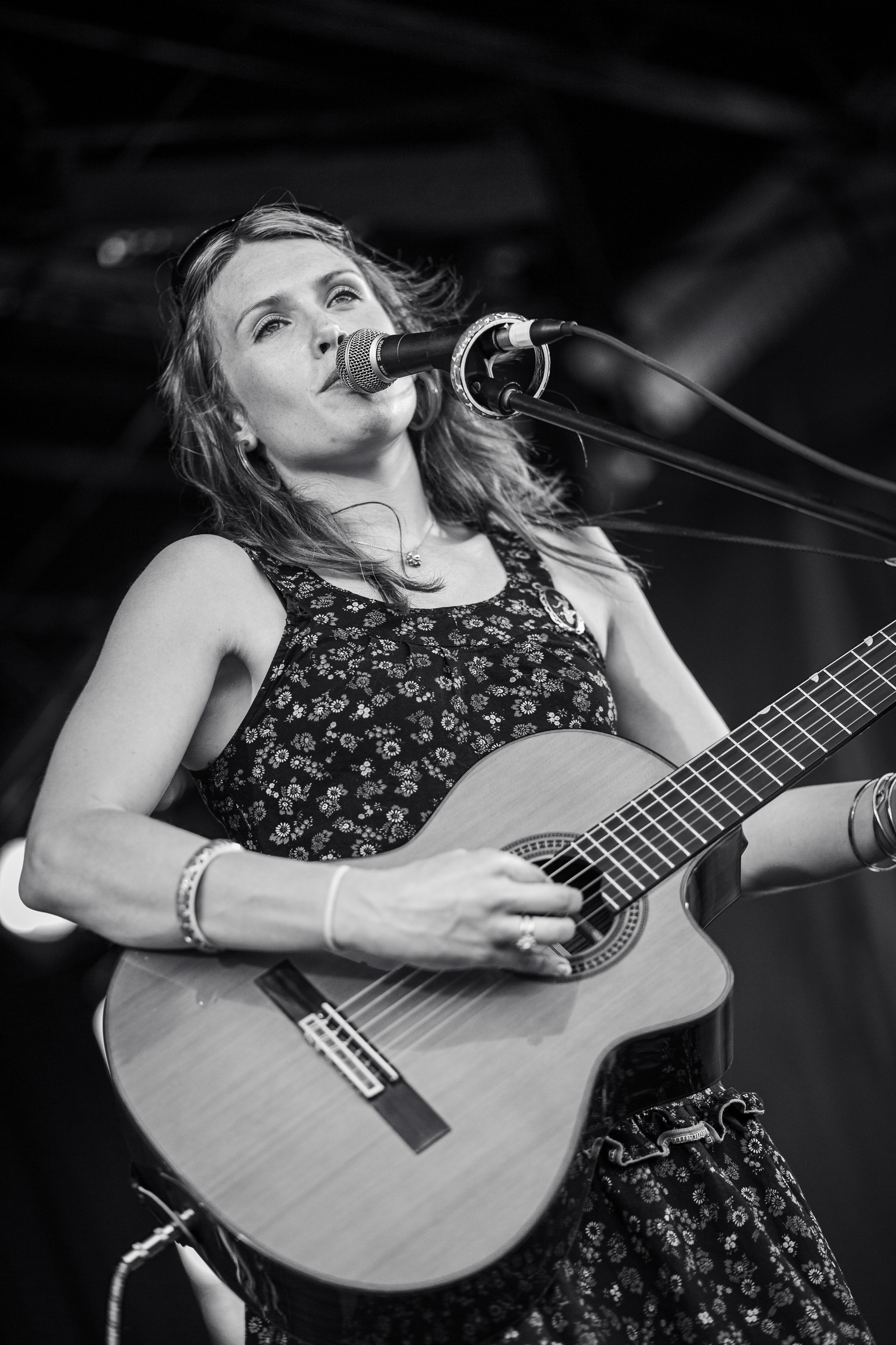 Clare Bowditch playing guitar and singing into a microphone at a music festival.