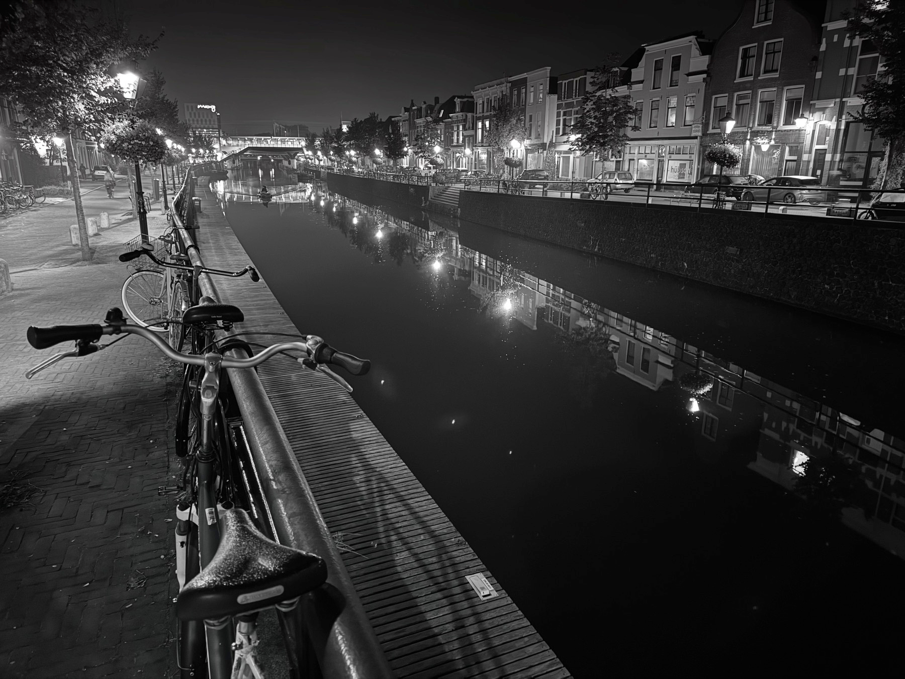 Monochrome night view of a canal, with a parked bike in the front